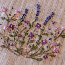 Load image into Gallery viewer, Close-up of a floral embroidered design on beige linen fabric, featuring pink and purple flowers with green stems and leaves.
