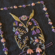 Load image into Gallery viewer, Close-up of an embroidered owl floral design on a dark fabric background, featuring purple flowers, green leaves, and gold accents.
